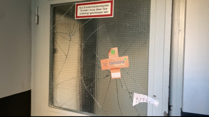 Eine Tür mit einer zerschlagenen Glasscheibe. Darauf ist ein Pflaster.